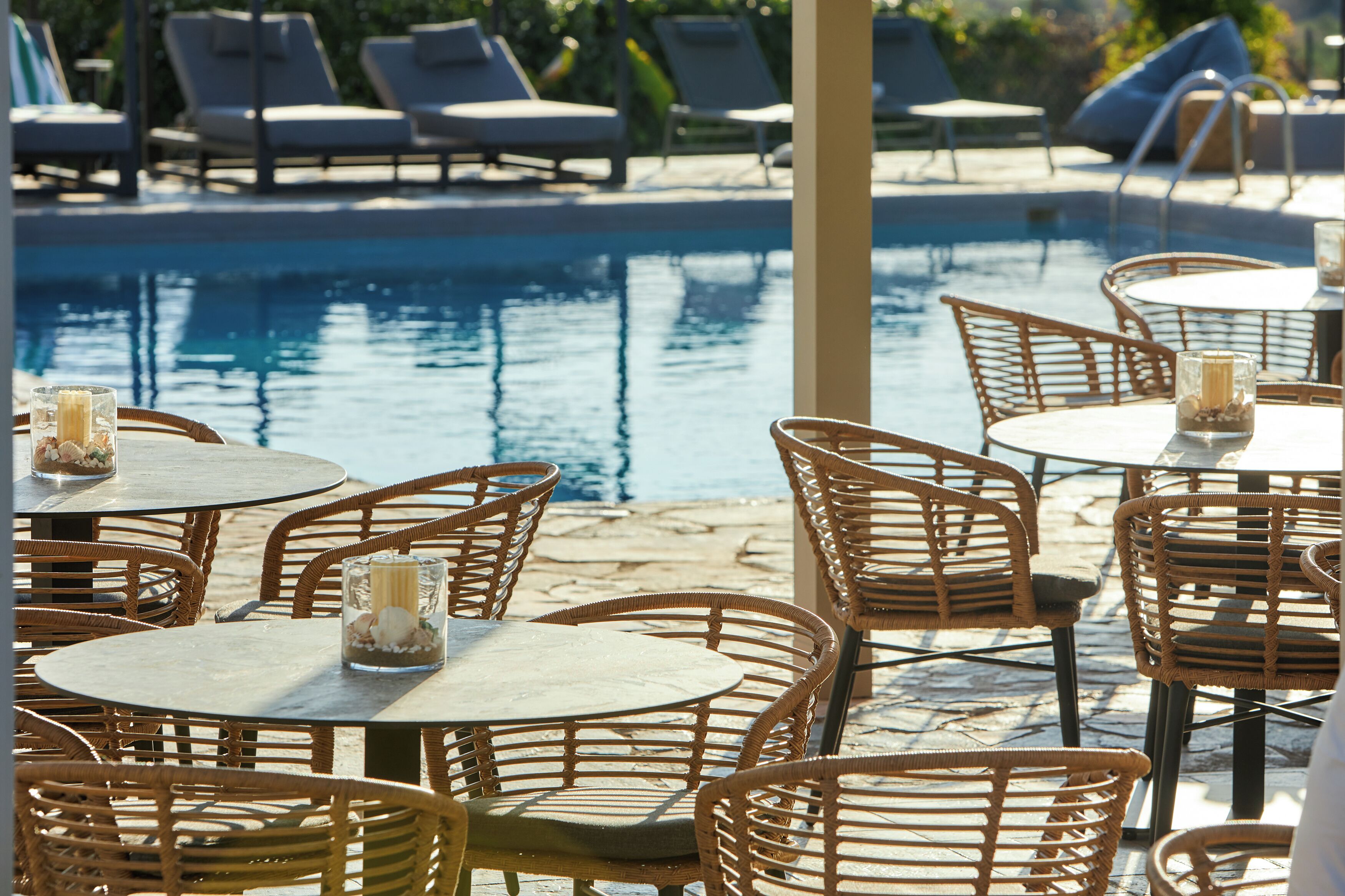 A poolside area with wicker chairs and tables, some with candles.