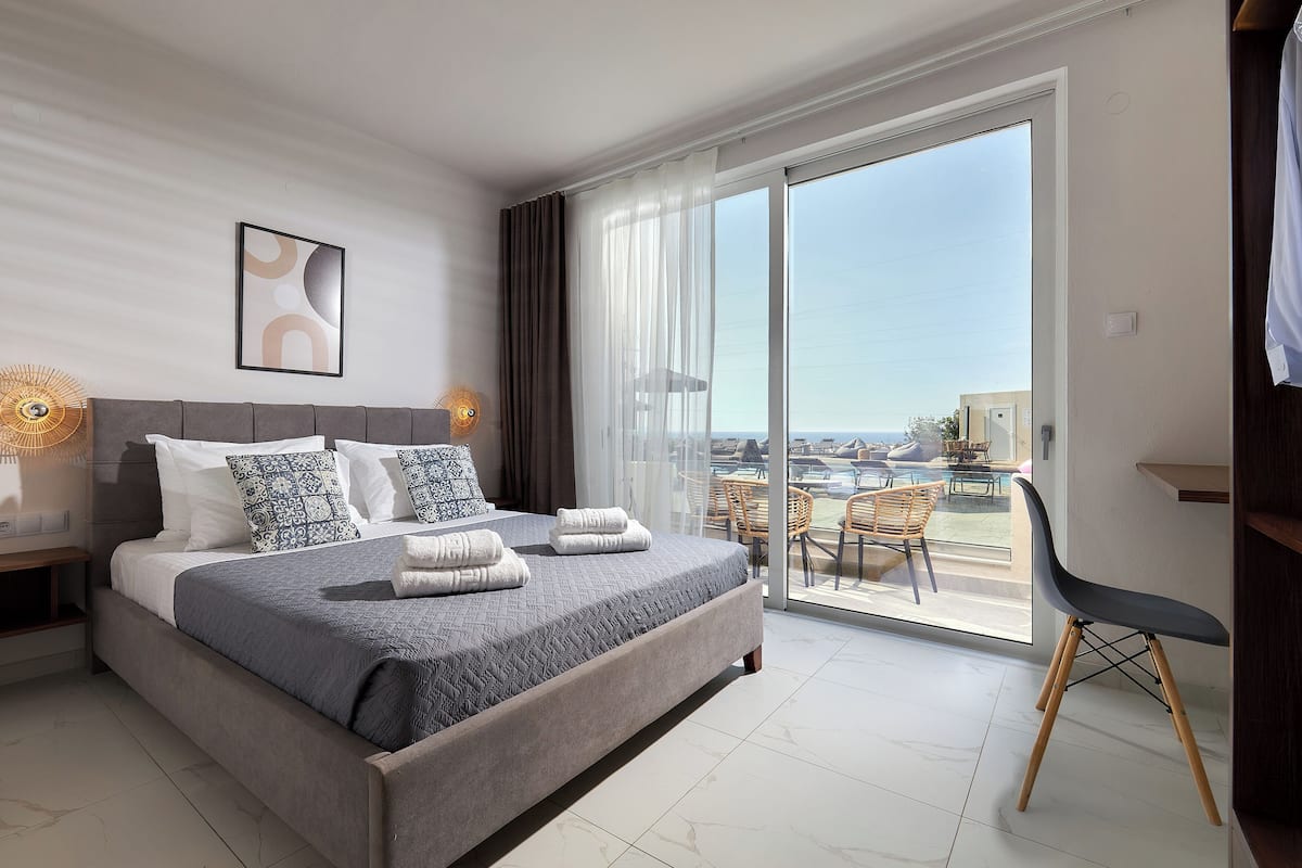 A modern hotel room with a large bed, a balcony with a view, and a desk area.
