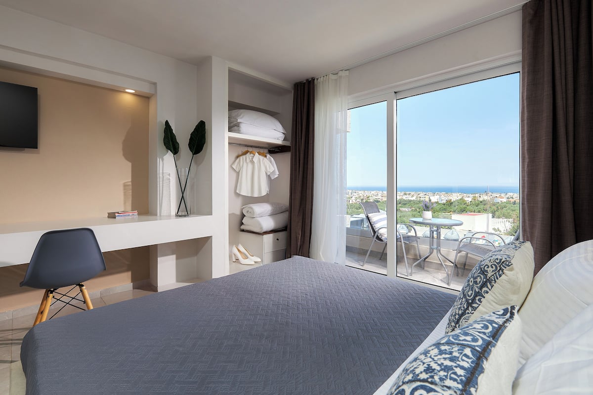 A hotel room with a large bed, a desk, and a balcony with a view of the city.