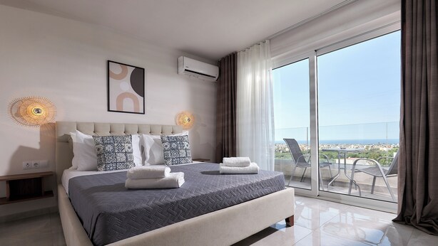 Una habitación de hotel moderna con una cama grande, vistas de la ciudad y un balcón con sillas.