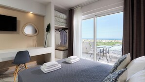 Habitación de hotel con cama, escritorio, silla, televisor, balcón con mesa y sillas, y vista a la ciudad.