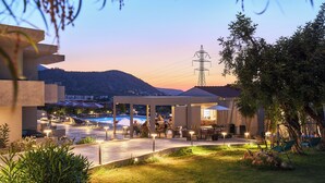 A poolside area with lounge chairs and tables, surrounded by greenery and a view of hills. - Mila Malia Suites (Hersonissos)
