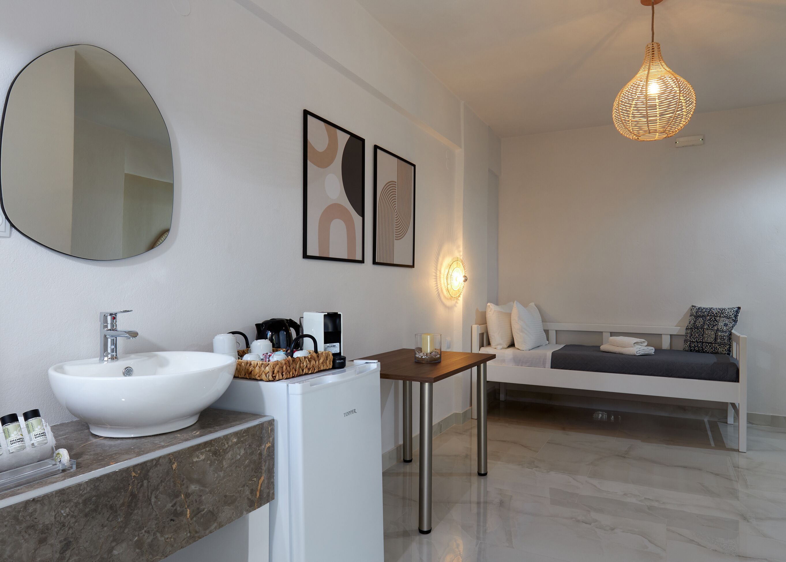 A modern bathroom with a large oval mirror, a white sink, and a coffee station.