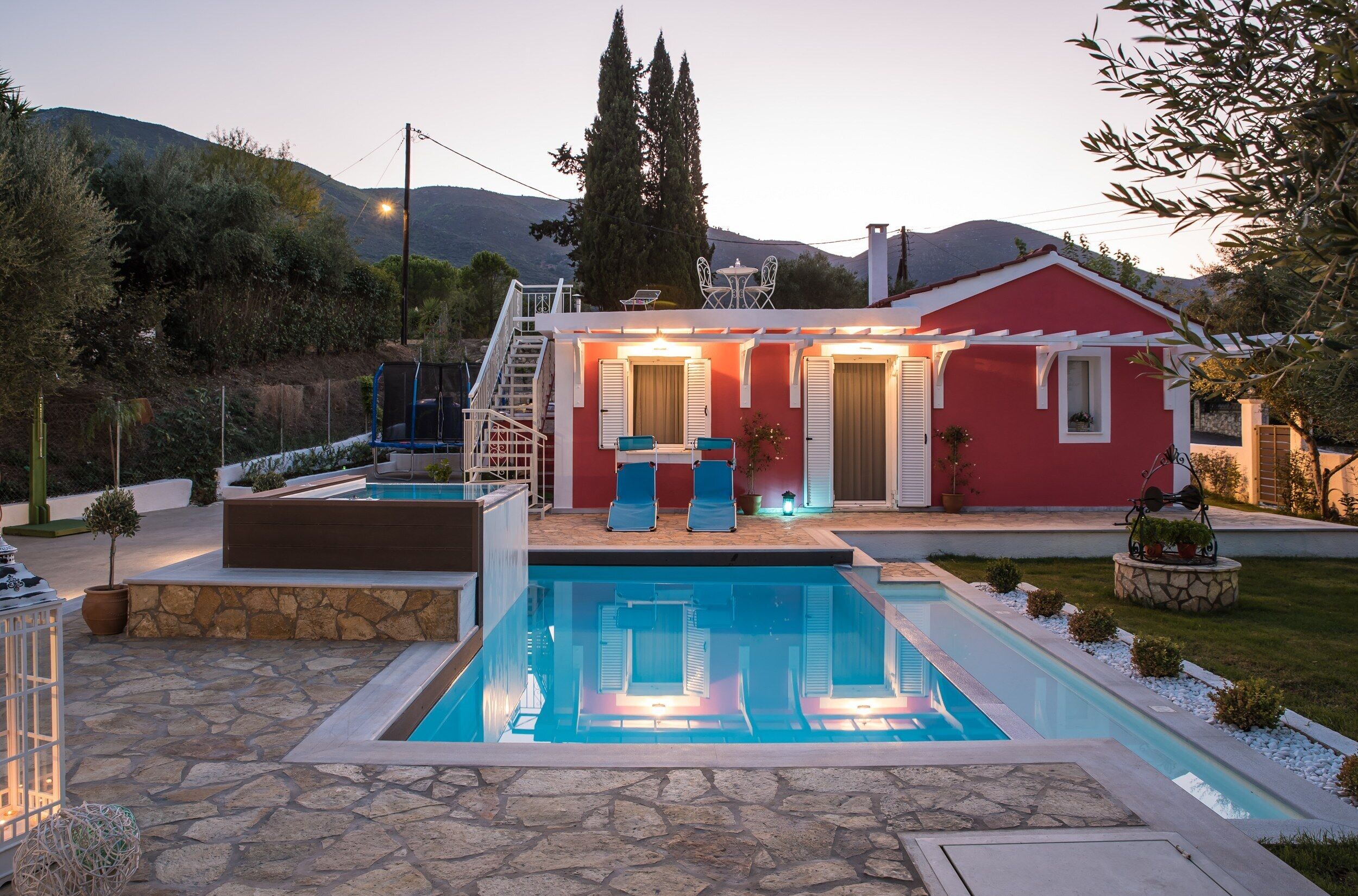 A red villa with a swimming pool, outdoor seating, and a staircase leading to the roof.