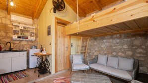Ein gemütliches Zimmer mit Steinwand, Holzboden, einer Couch, einem kleinen Tisch, einem Ventilator und einer Küchenzeile.