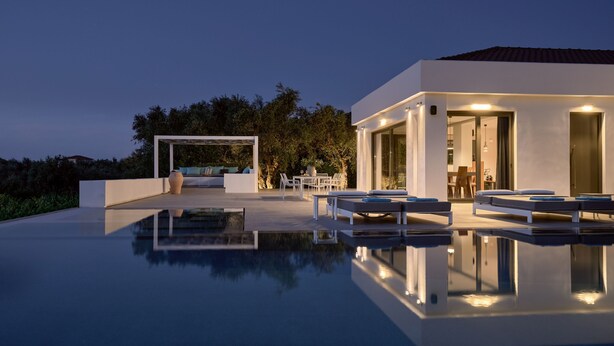 A modern outdoor pool area with lounge chairs and a seating area, surrounded by a well-maintained garden and a building with large windows.