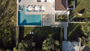 An aerial view of a property with a swimming pool, lounge area with umbrellas, and a garden.