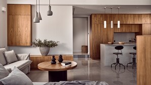 A modern living room with a sofa, coffee table, and a potted plant. There is a kitchen area with wooden cabinets and bar stools.