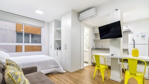 A compact hotel room with a bed, a sofa, a desk with a chair, a TV, and a kitchenette. - Av1110 Studio Avanhandava (São Paulo)