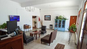 A spacious living room with a TV, sofa, and coffee table. There is a blue cabinet with plants and a door marked with the number 8. - Hostal Tilian (Salta)