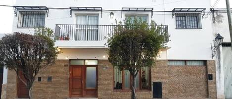 Un edificio de dos pisos con puerta de madera, un balcón y fachada de ladrillo.