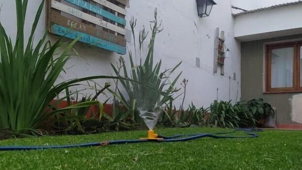 A well-maintained lawn with a sprinkler system, a wall with a signboard, and potted plants. - Hostal Tilian (Salta)