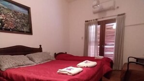 A bedroom with a double bed, a chair, a painting on the wall, and a window with curtains. - Hostal Tilian (Salta)