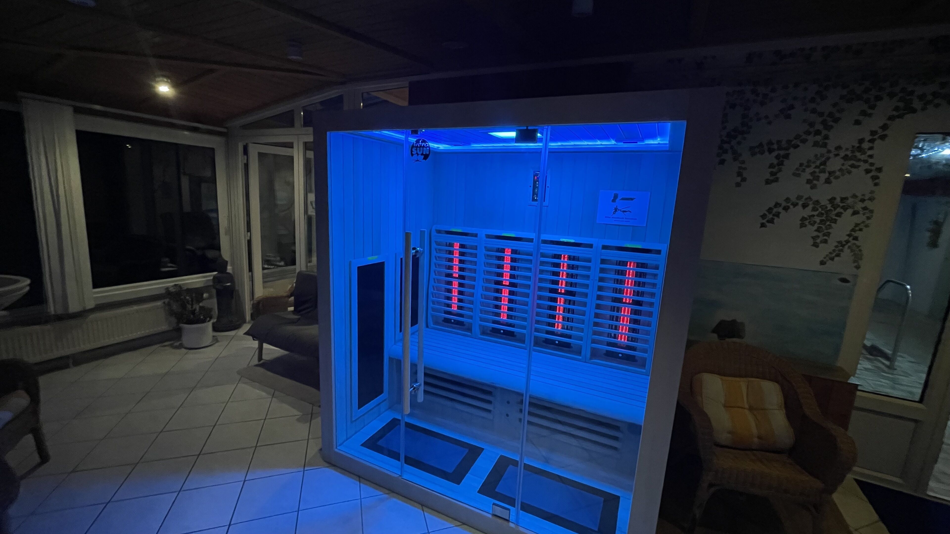 Habitación con cerramiento de vidrio que contiene una unidad de calefacción con luces rojas, un sofá, una silla y una ventana con vista al exterior.