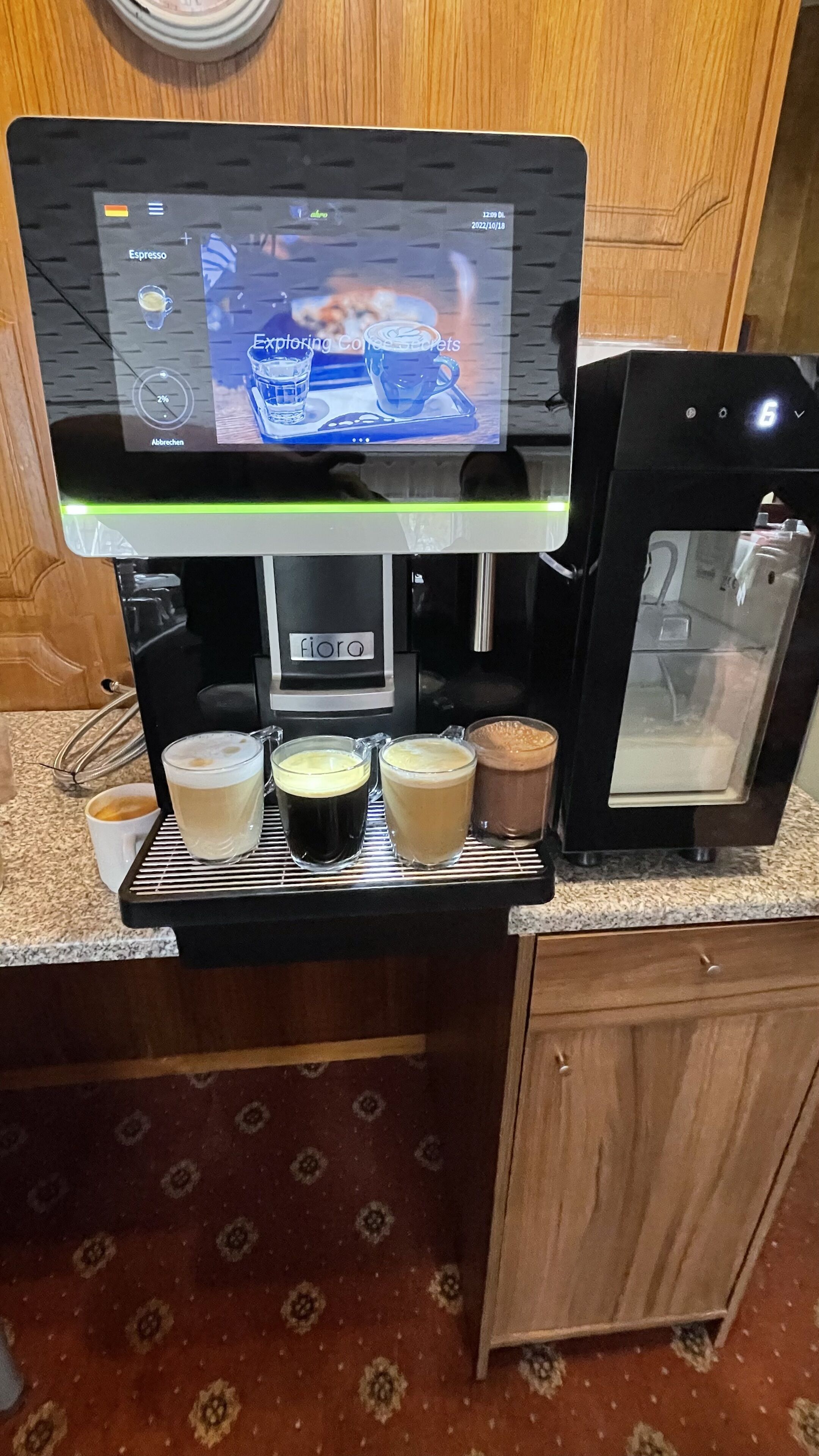 Une machine à café dotée d’un écran numérique, avec quatre tasses de café posées sur le comptoir.