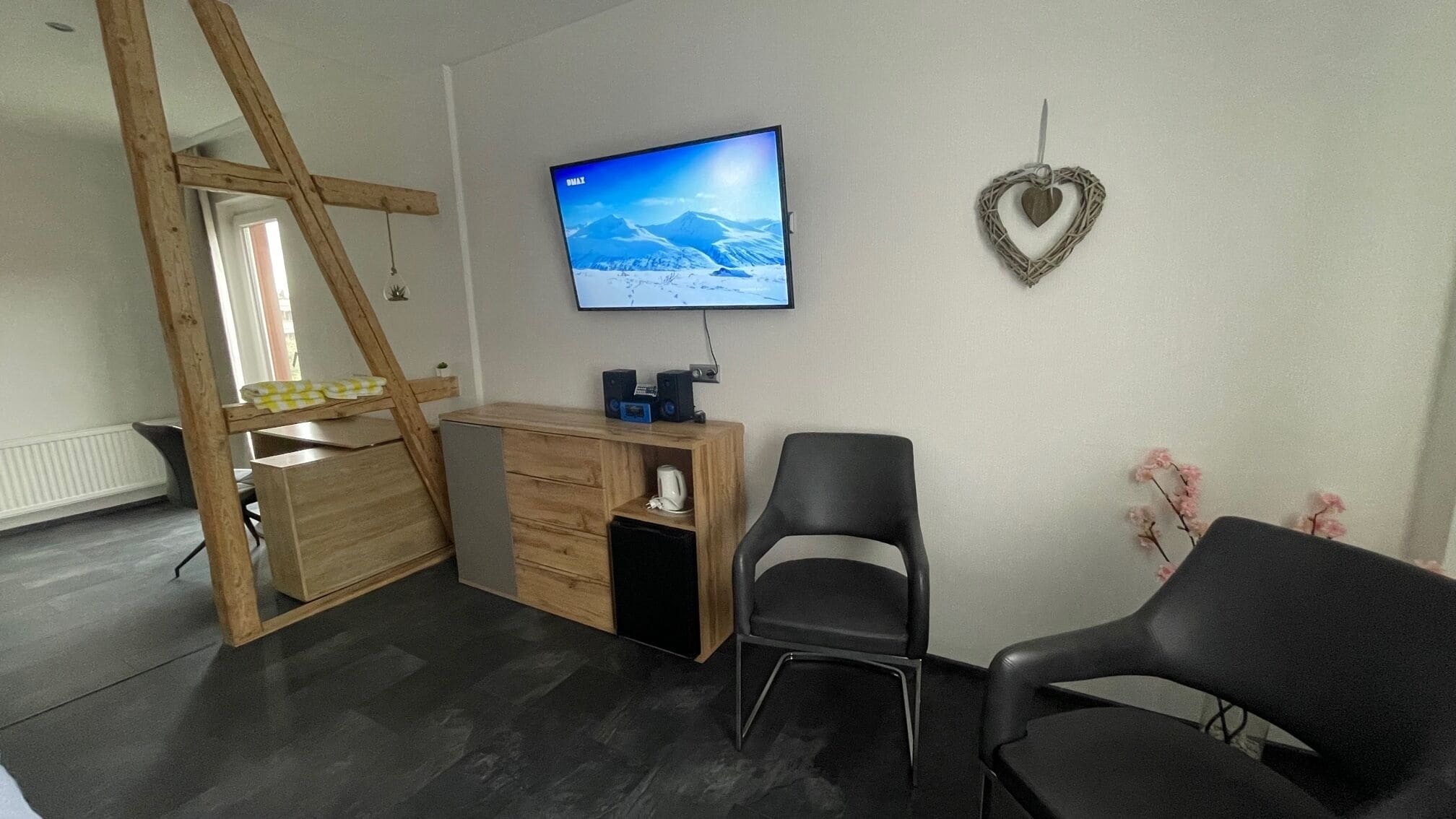 A room with a desk, two chairs, a TV on the wall, and a heart-shaped decoration.