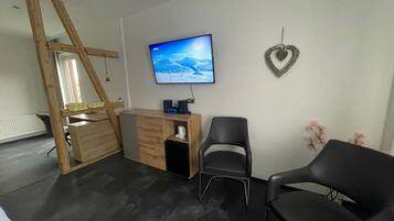 Ein Zimmer mit Schreibtisch, zwei Stühlen, einem Fernseher an der Wand und einer herzförmigen Dekoration.