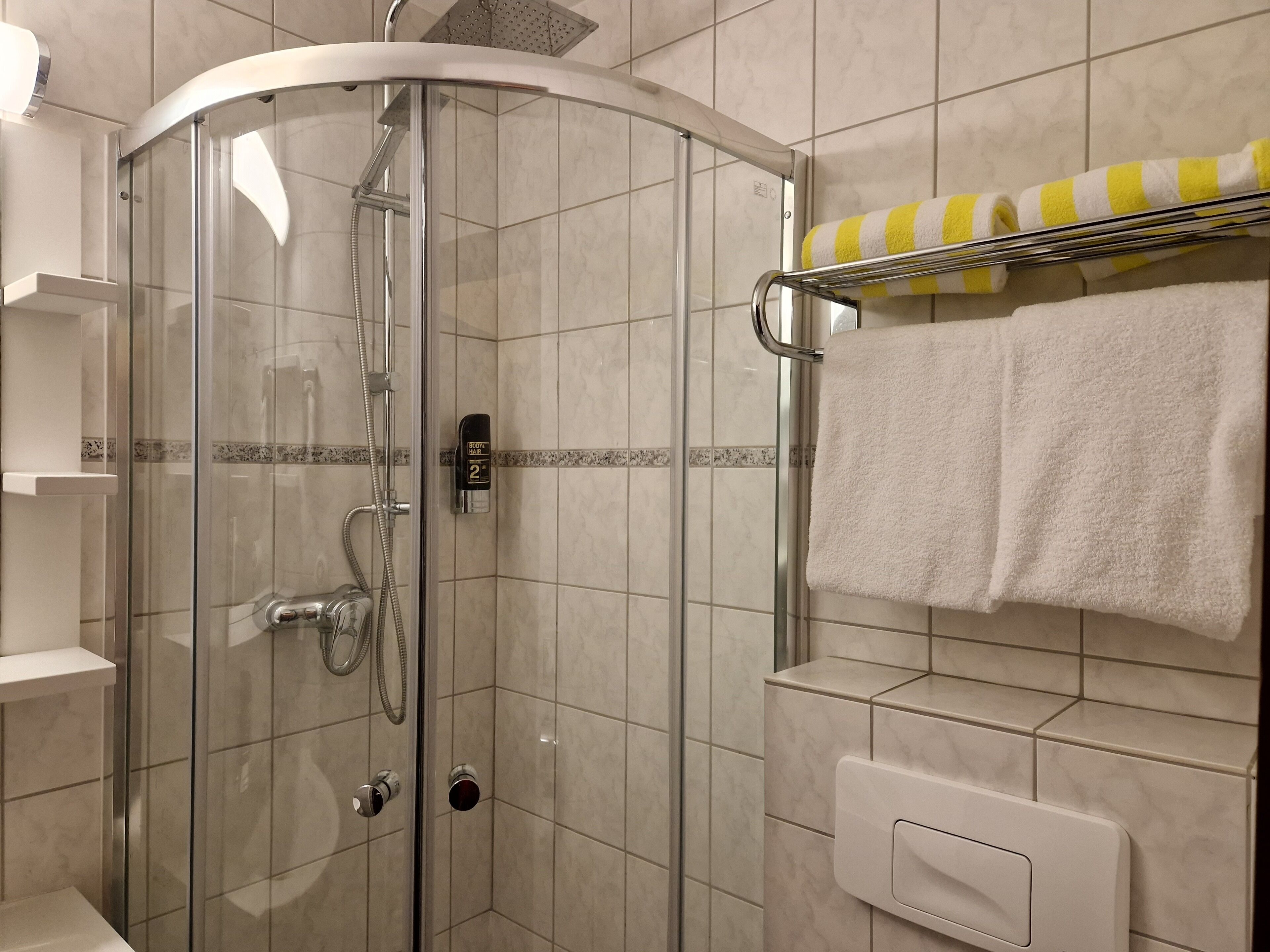 A modern bathroom with a glass-enclosed shower, a towel rack with striped towels, and a soap dispenser.