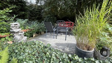 Un patio con una fuente de piedra, sillas de metal y plantas en macetas.