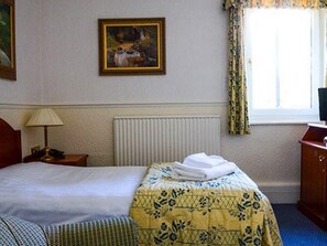 A hotel room with a bed, a nightstand, a lamp, a painting on the wall, and a window with curtains. - The Clarkes Hotel (Barrow-in-Furness)