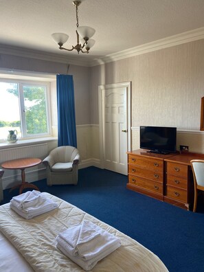 A hotel room with a bed, a television, a dresser, a chair, a small table, and a window with curtains. - The Clarkes Hotel (Barrow-in-Furness)