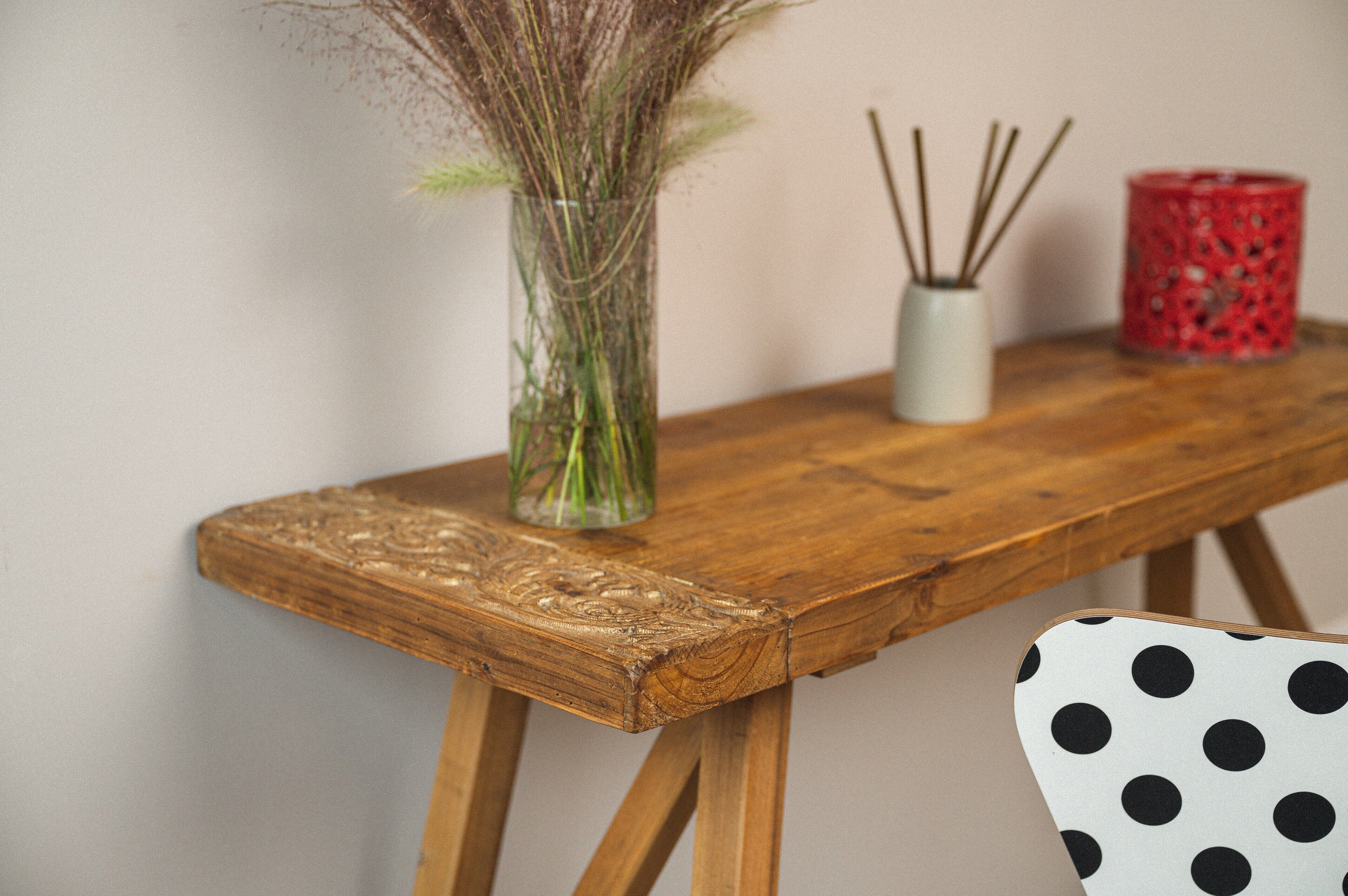 Una mesa de madera con un jarrón de plantas secas, un candelabro blanco y una vela roja.