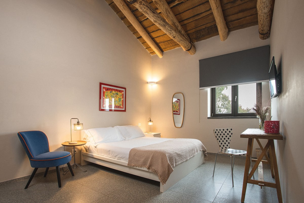 Une chambre à coucher avec un lit, une chaise, une petite table, un miroir et une fenêtre.