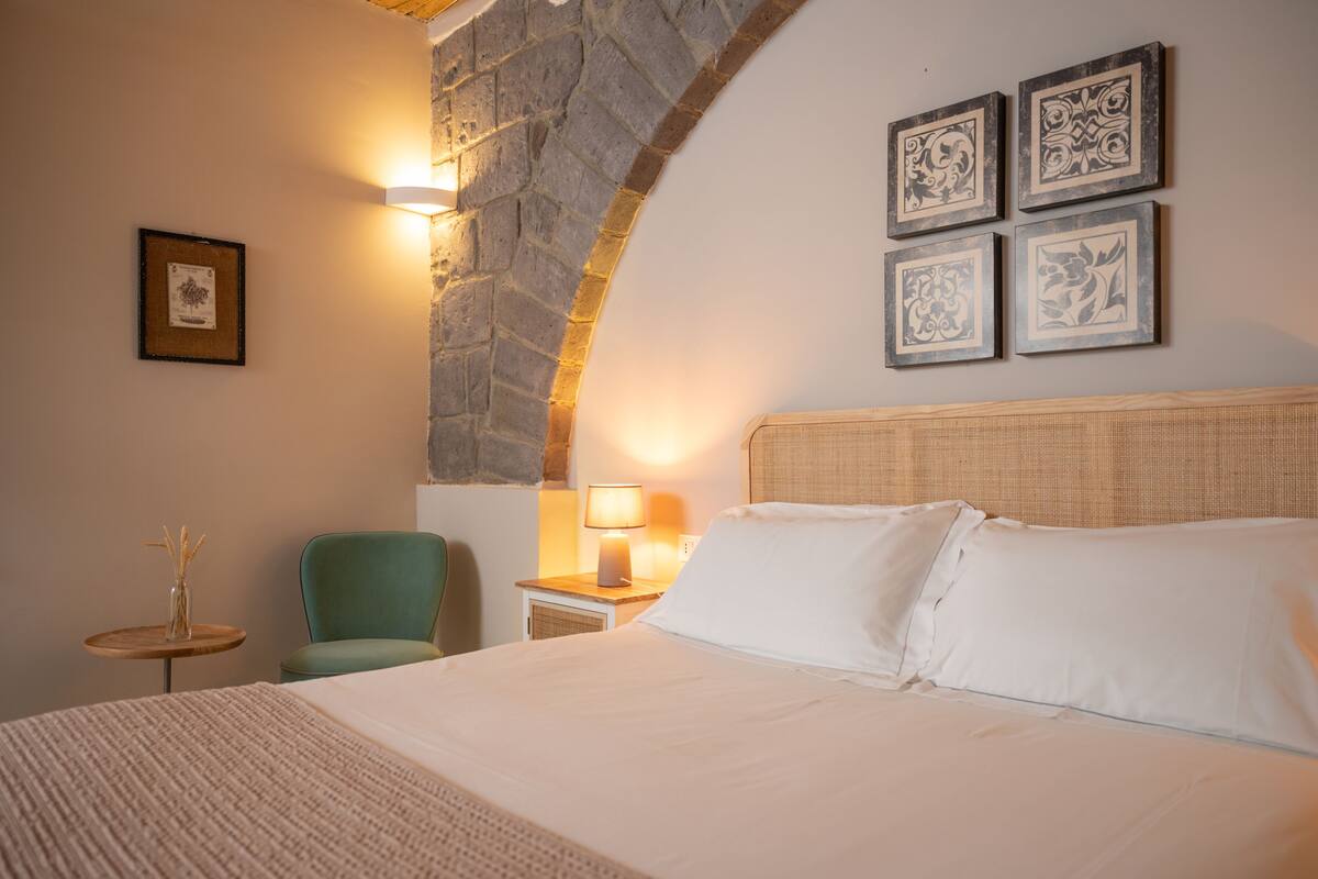 Une chambre d’hôtel avec un lit, une chaise, une petite table avec une lampe et des œuvres d’art encadrées accrochées au mur.