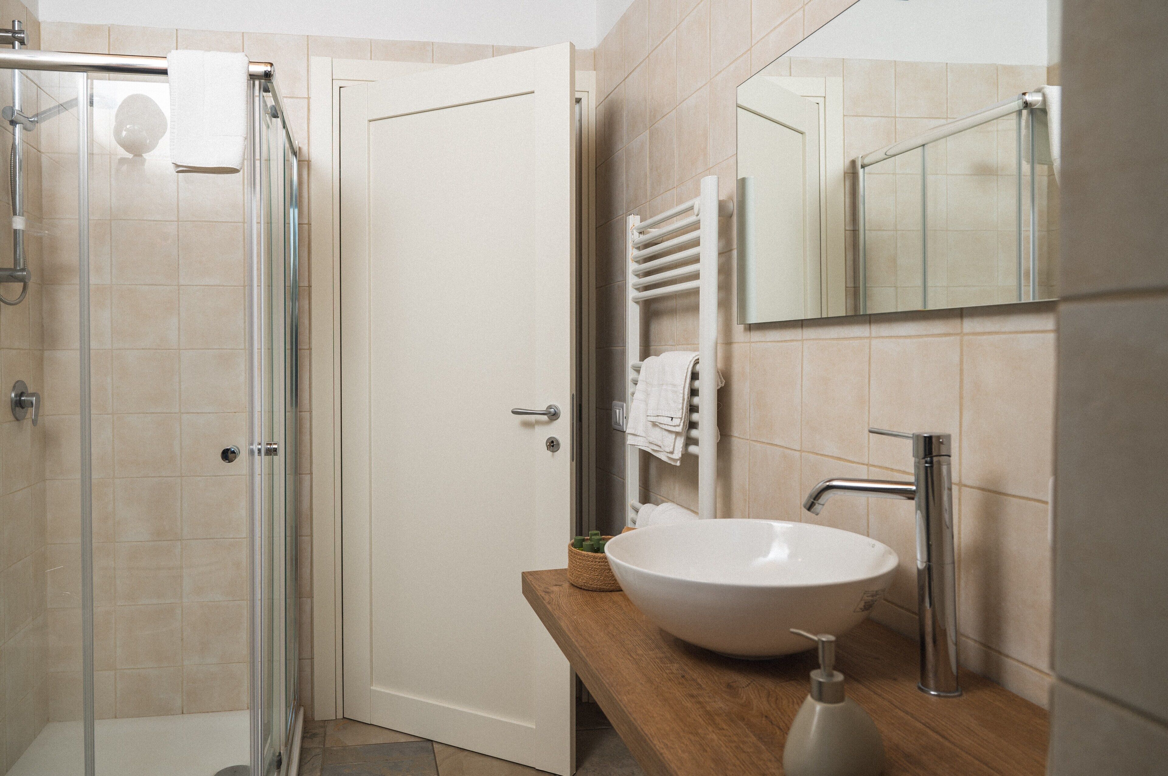 Une salle de bain moderne avec une douche à parois de verre, un lavabo blanc doté d’un distributeur de savon et un porte-serviettes avec des serviettes.