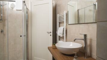 Une salle de bain moderne avec une douche à parois de verre, un lavabo blanc doté d’un distributeur de savon et un porte-serviettes avec des serviettes.