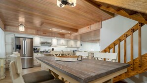 A modern kitchen with wooden cabinets, a stainless steel refrigerator, and a wooden dining table with chairs. - Exquisite 2 Story Penthouse with Spectacular Views of the Ocean and the Bay (Ocean City)