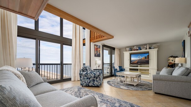 A spacious living room with a large window, a blue patterned armchair, a grey sofa, and a flat-screen TV on a white cabinet. - Exquisite 2 Story Penthouse with Spectacular Views of the Ocean and the Bay (Ocean City)