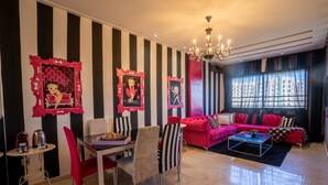 Una sala de estar con pared a rayas, un juego de sofá rojo, una mesa de comedor con sillas y una araña.