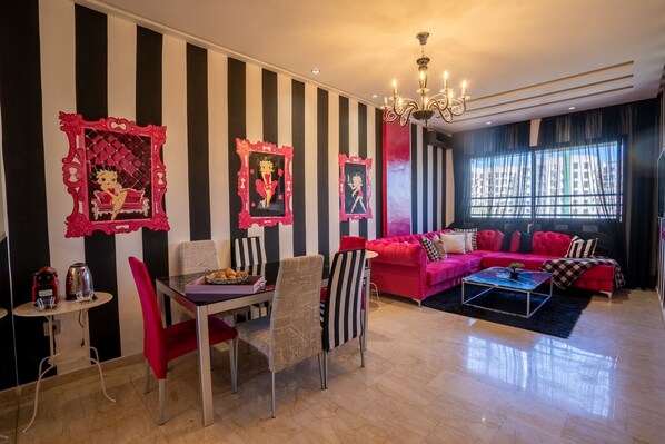 A living room with a striped wall, a red sofa set, a dining table with chairs, and a chandelier. - Chez Betty with rooftop Swimming pool (Casablanca)