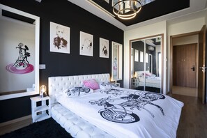 A modern bedroom with a large bed, a white headboard, and a black and white patterned bedspread. There are three framed artworks on the wall, a small bedside table with a lamp, and a large mirror reflecting the room. - Chez Betty with rooftop Swimming pool (Casablanca)