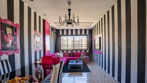 Un salón moderno con un diseño de pared a rayas, una araña y un ventanal con vistas a edificios.