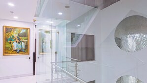 A modern interior with a glass staircase, a large painting on the wall, and decorative circular mirrors. - Amber Inn by Orion Hotels (New Delhi)