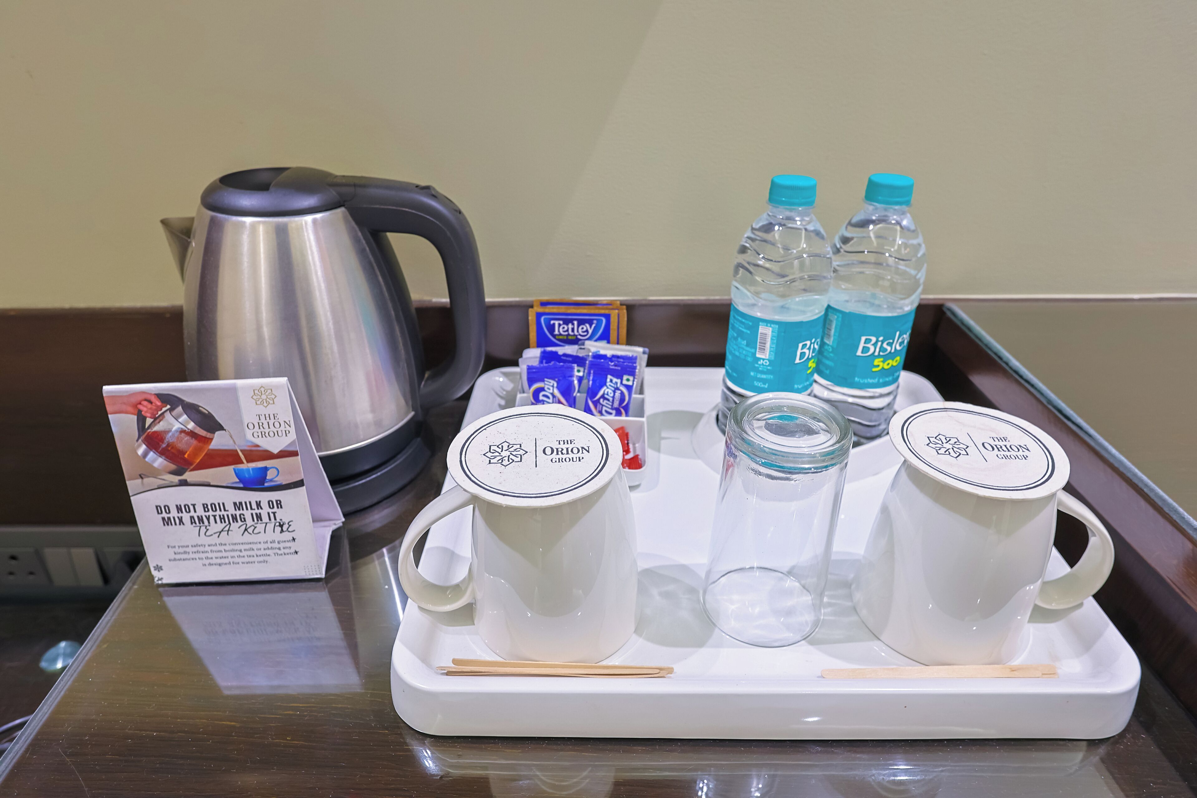 A tray with a teapot, two water bottles, a tea bag, and two white cups on a hotel table.