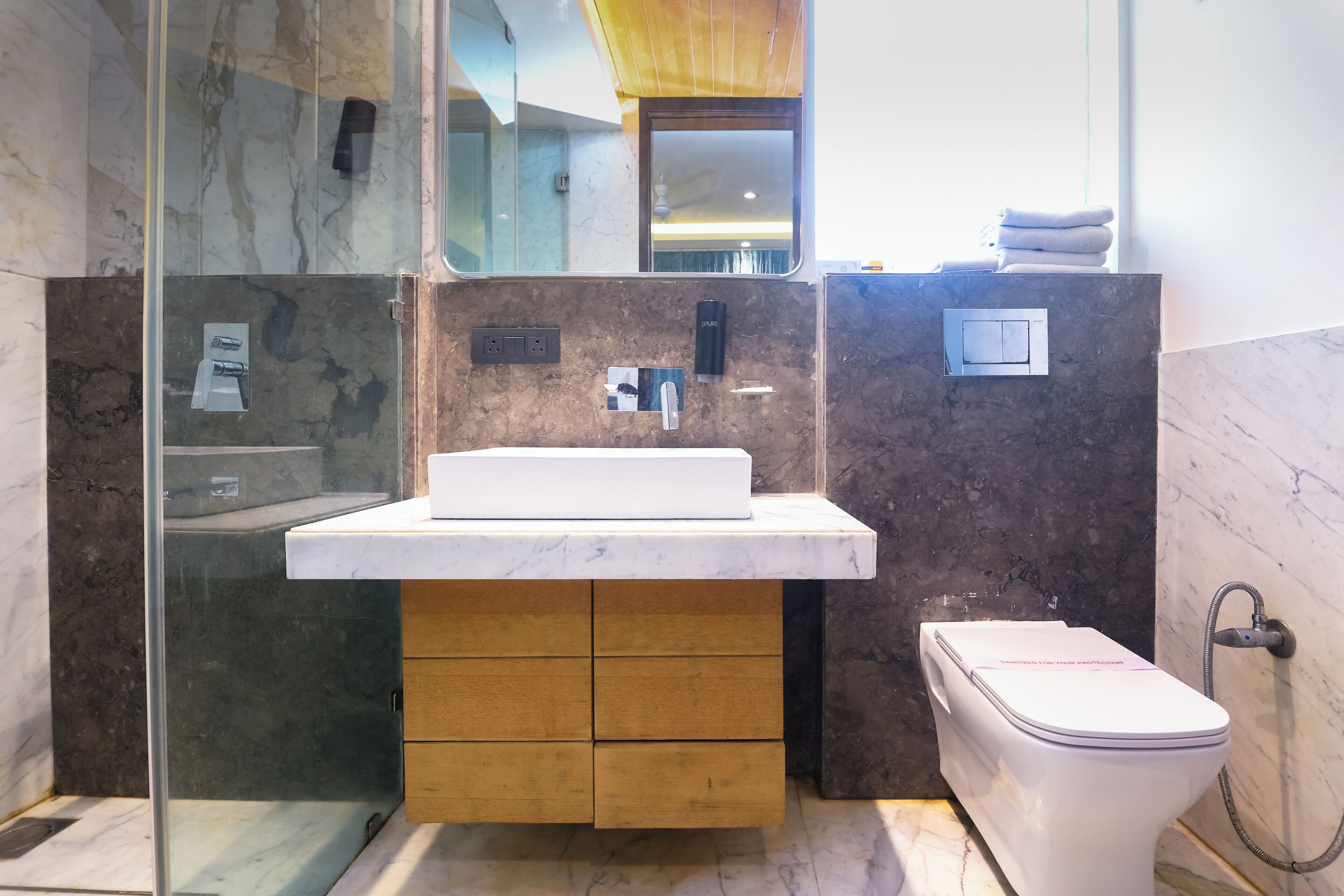 A modern bathroom with a marble sink, wooden cabinets, a toilet, and a glass shower enclosure.