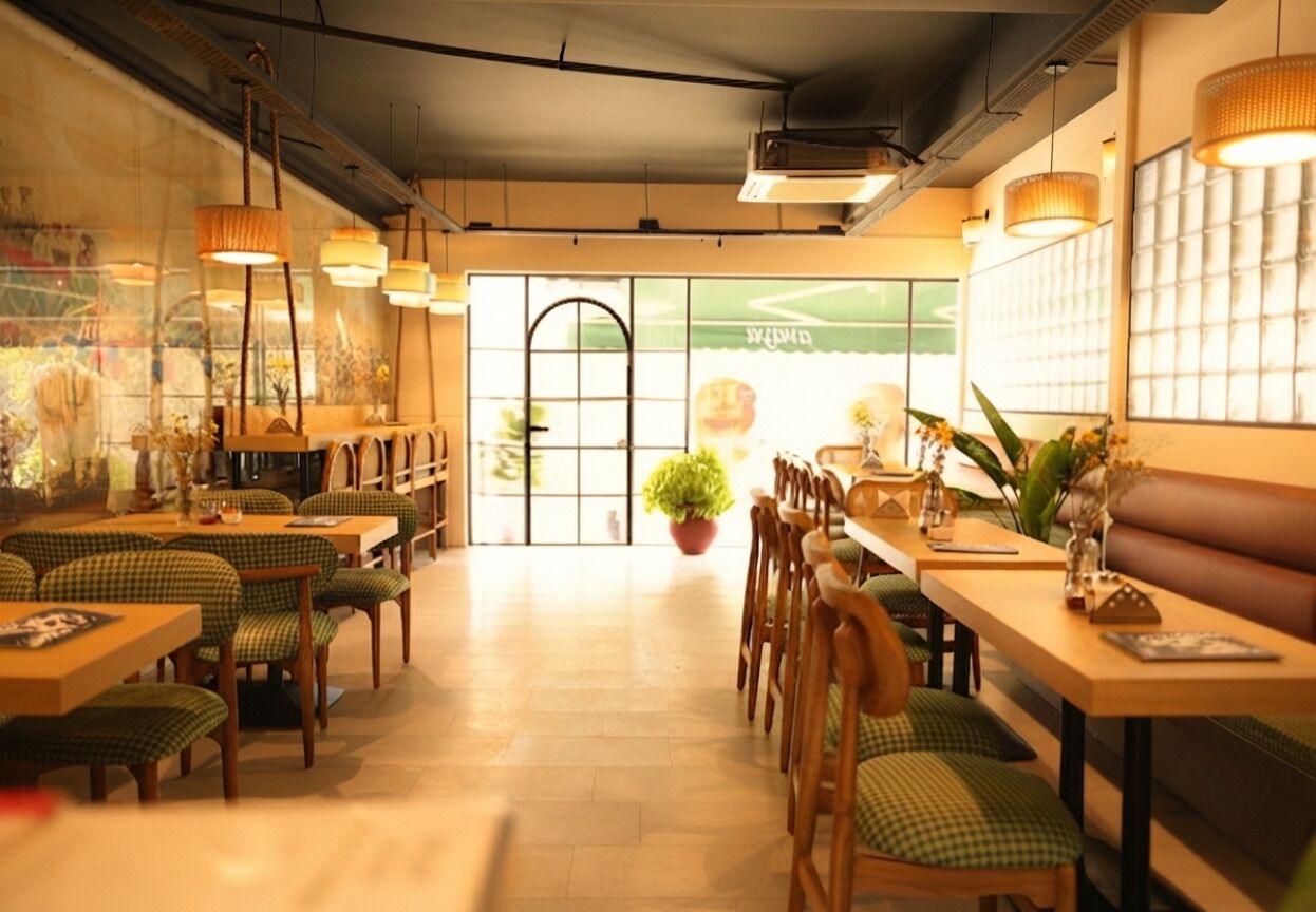 Interior de restaurante con mesas y sillas de madera, lámparas colgantes y un amplio ventanal con vistas.