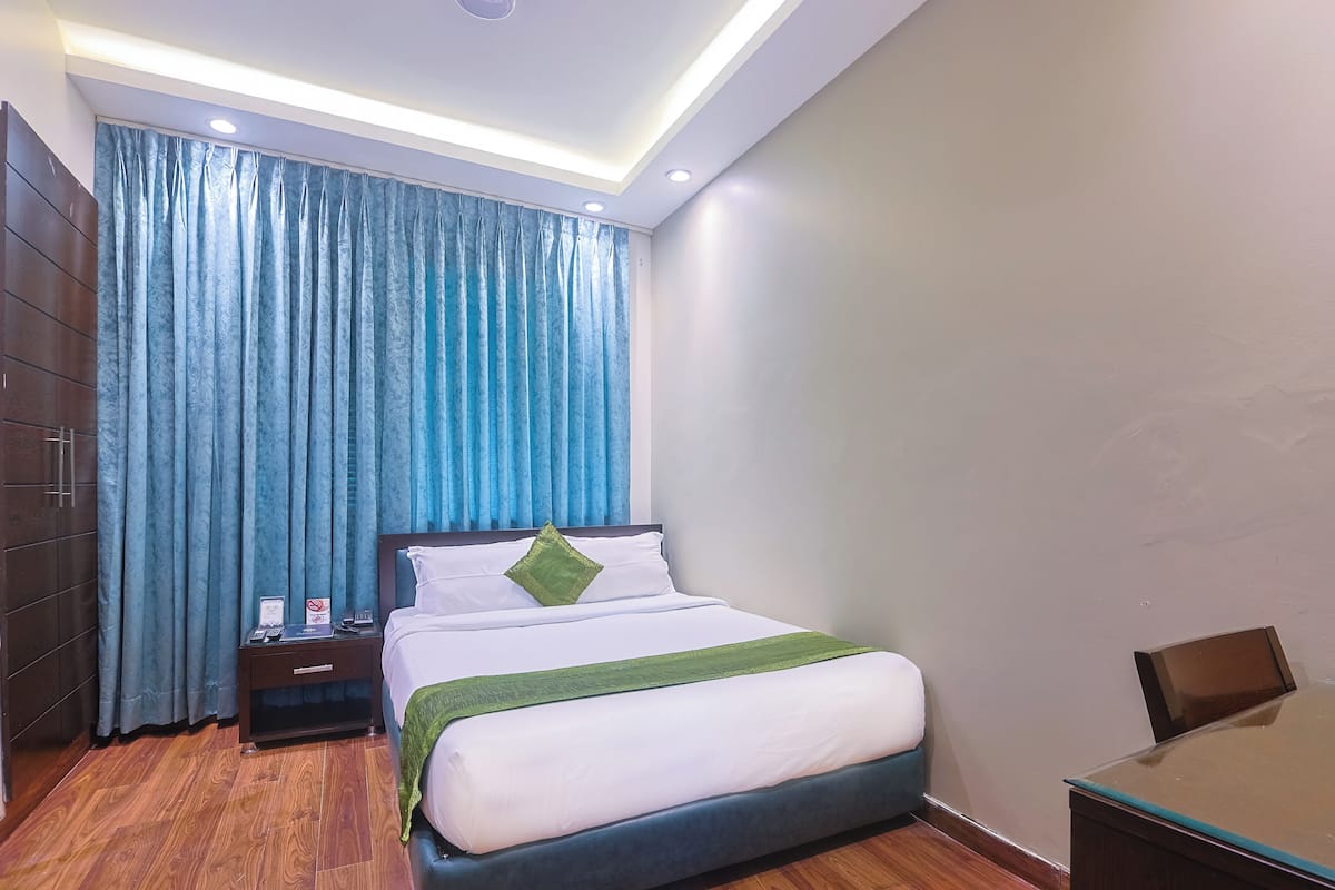 A hotel room with a bed, nightstand, and a desk with a chair.