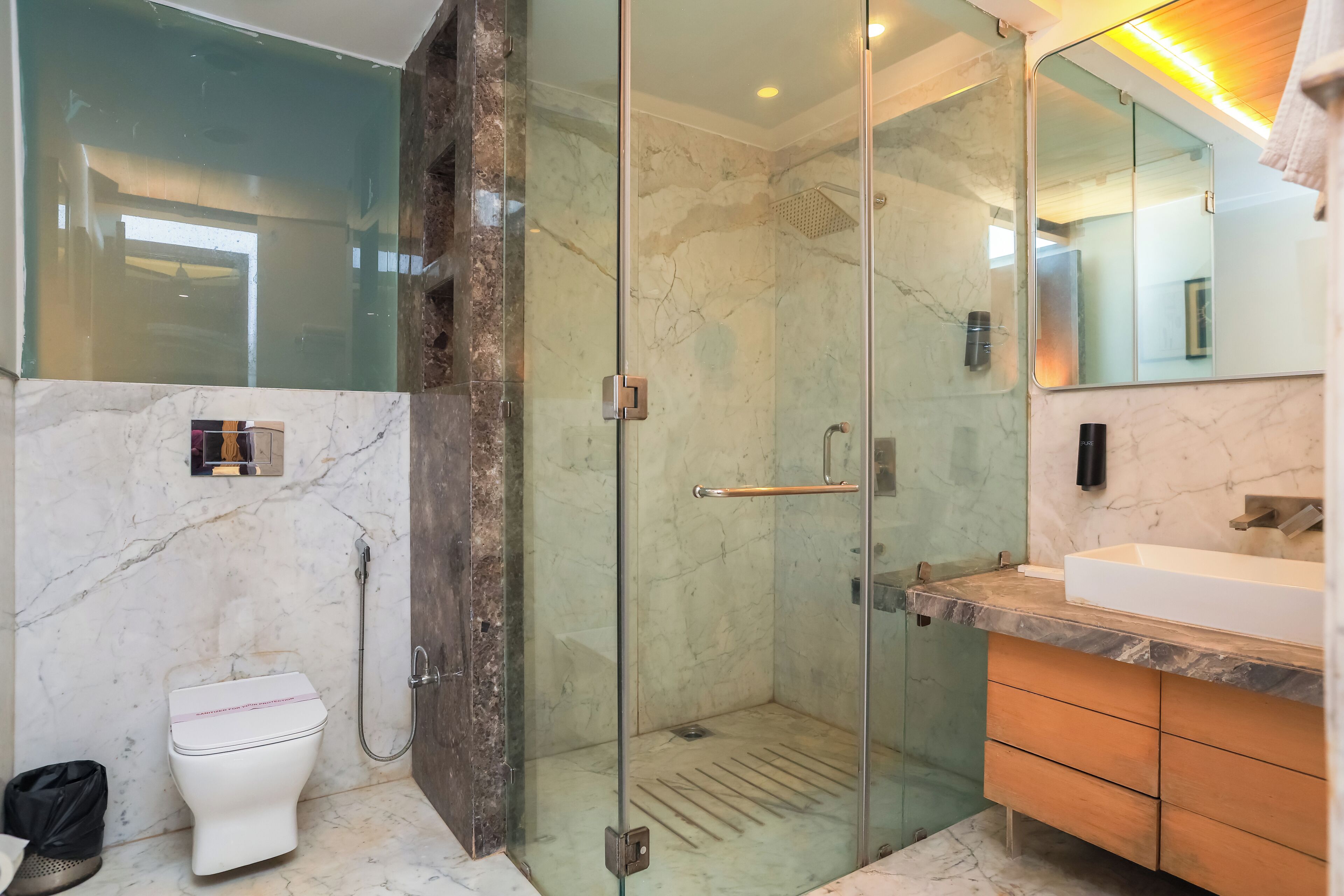 A modern bathroom with a glass-enclosed shower, a white toilet, and a vanity with a large mirror.