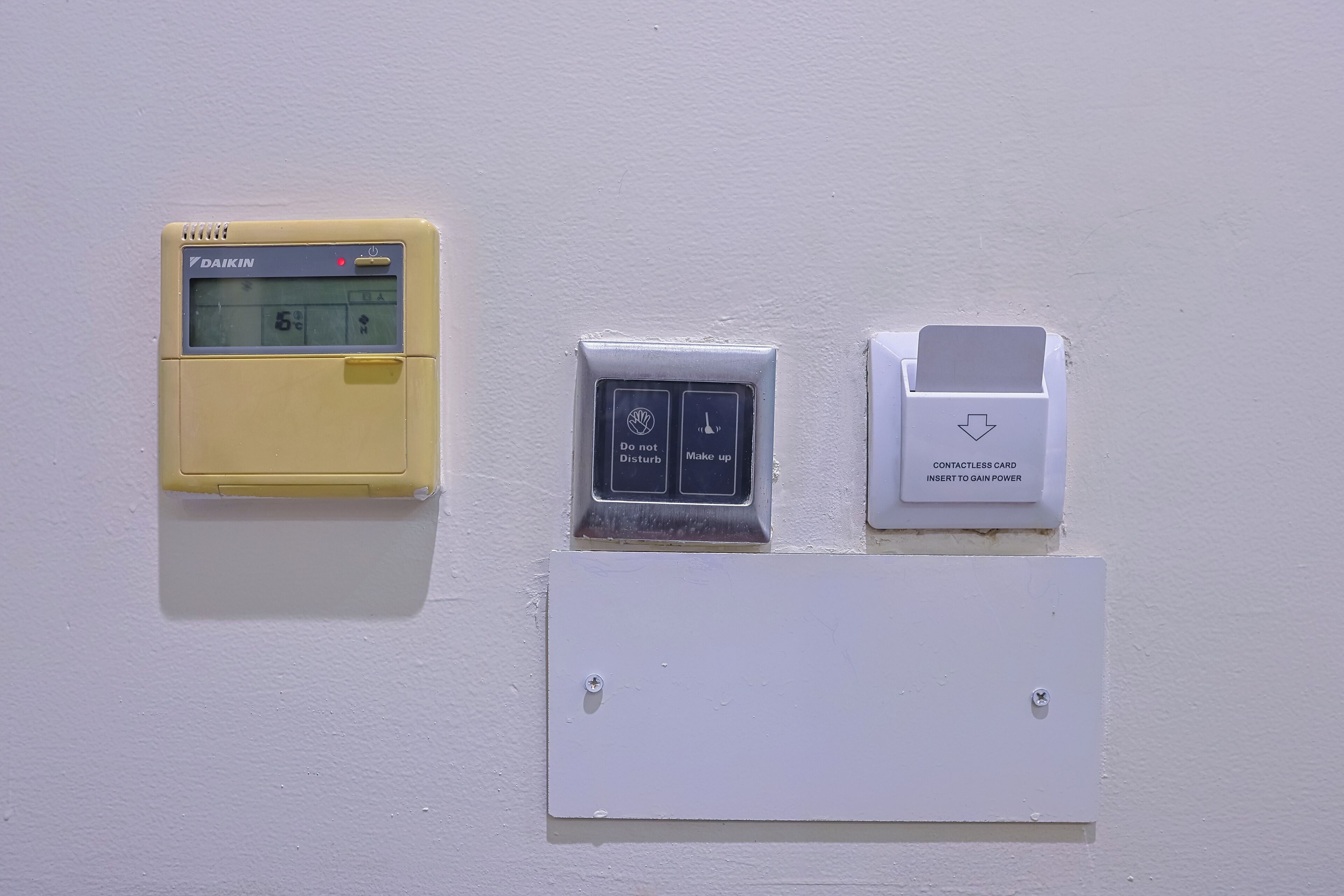 Un termostato fijado a la pared, un panel de control digital y un lector de tarjetas sin contacto.