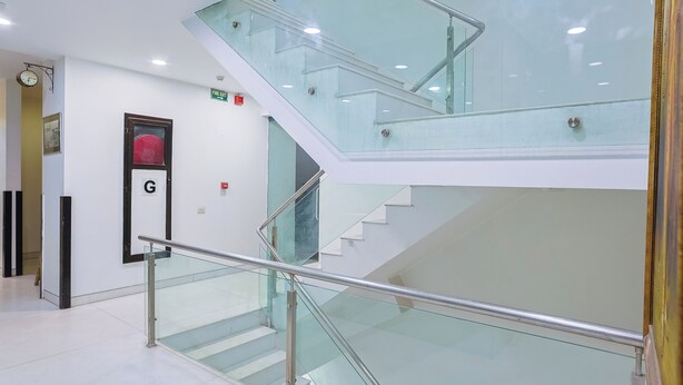 A modern interior with a glass staircase, a fire exit sign, and a door marked with a 'G'. - Amber Inn by Orion Hotels (New Delhi)