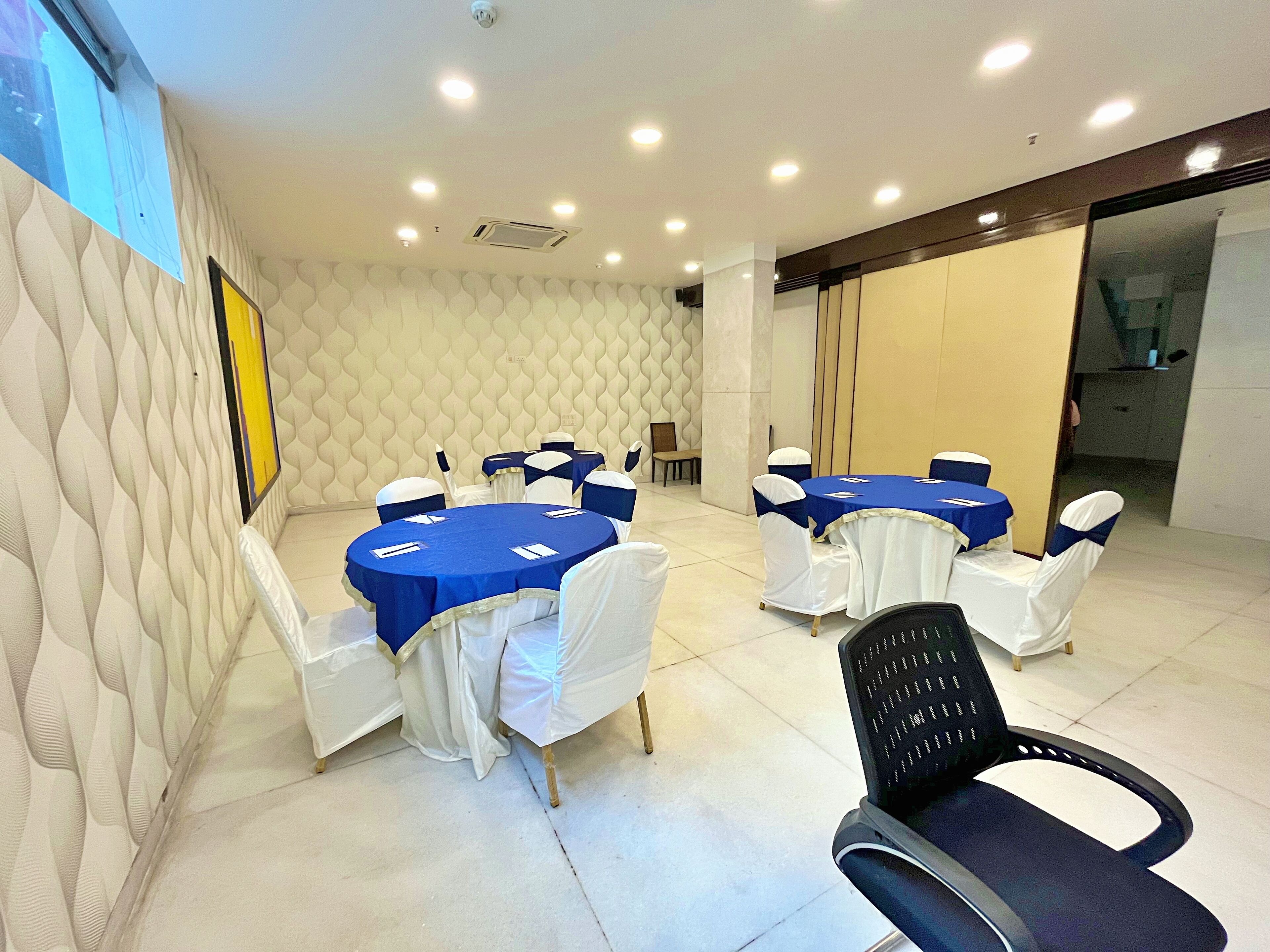 Un salón de conferencias con mesas redondas, sillas blancas y manteles azules.