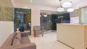 A modern reception area with a sofa, a checkered chair, and a reception desk. - Amber Inn by Orion Hotels (New Delhi)