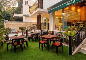 An outdoor seating area with tables and chairs, a staircase, and a building entrance with a sign. - Amber Inn by Orion Hotels (New Delhi)