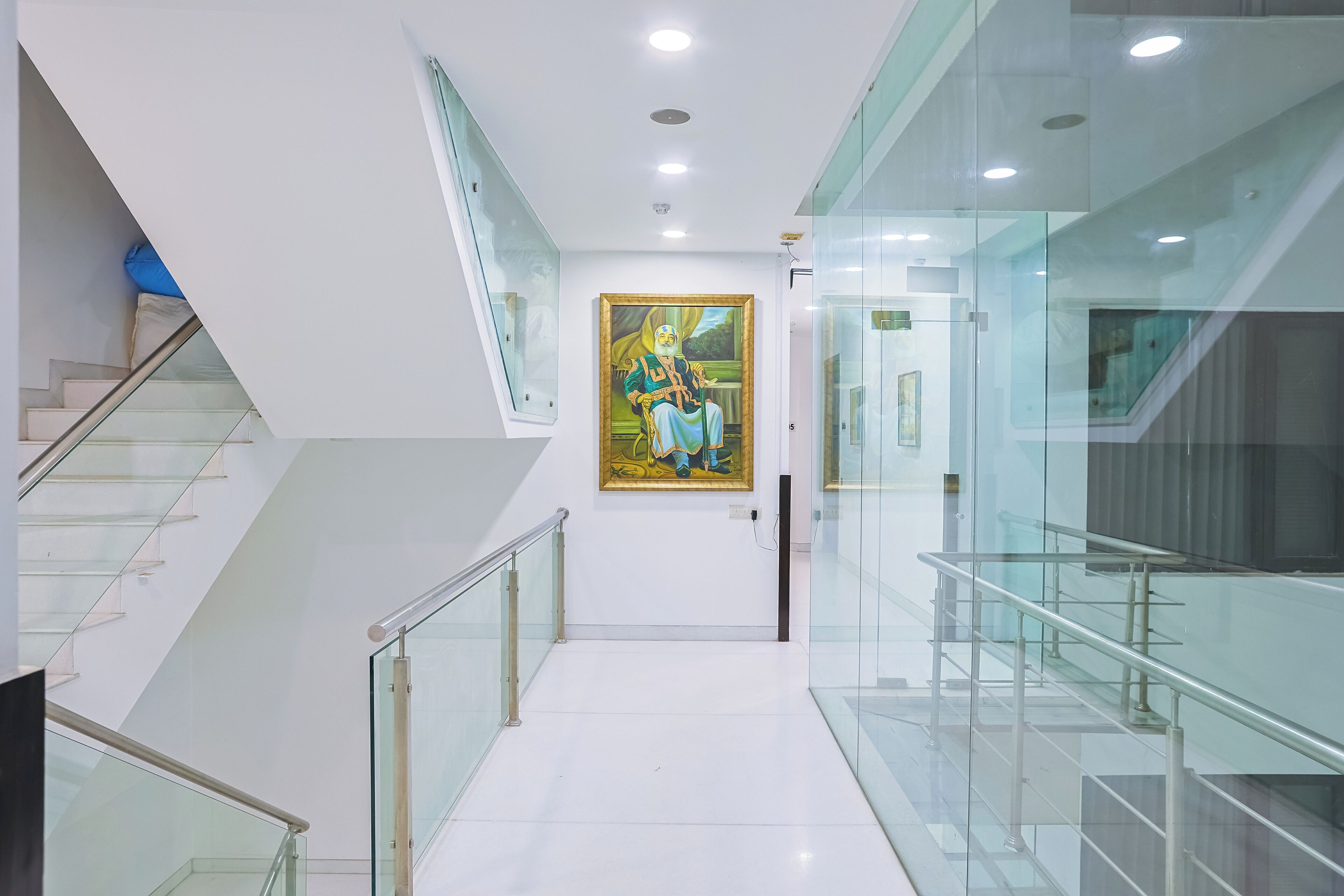 A modern interior with a glass staircase, a painting on the wall, and a clean, white floor.