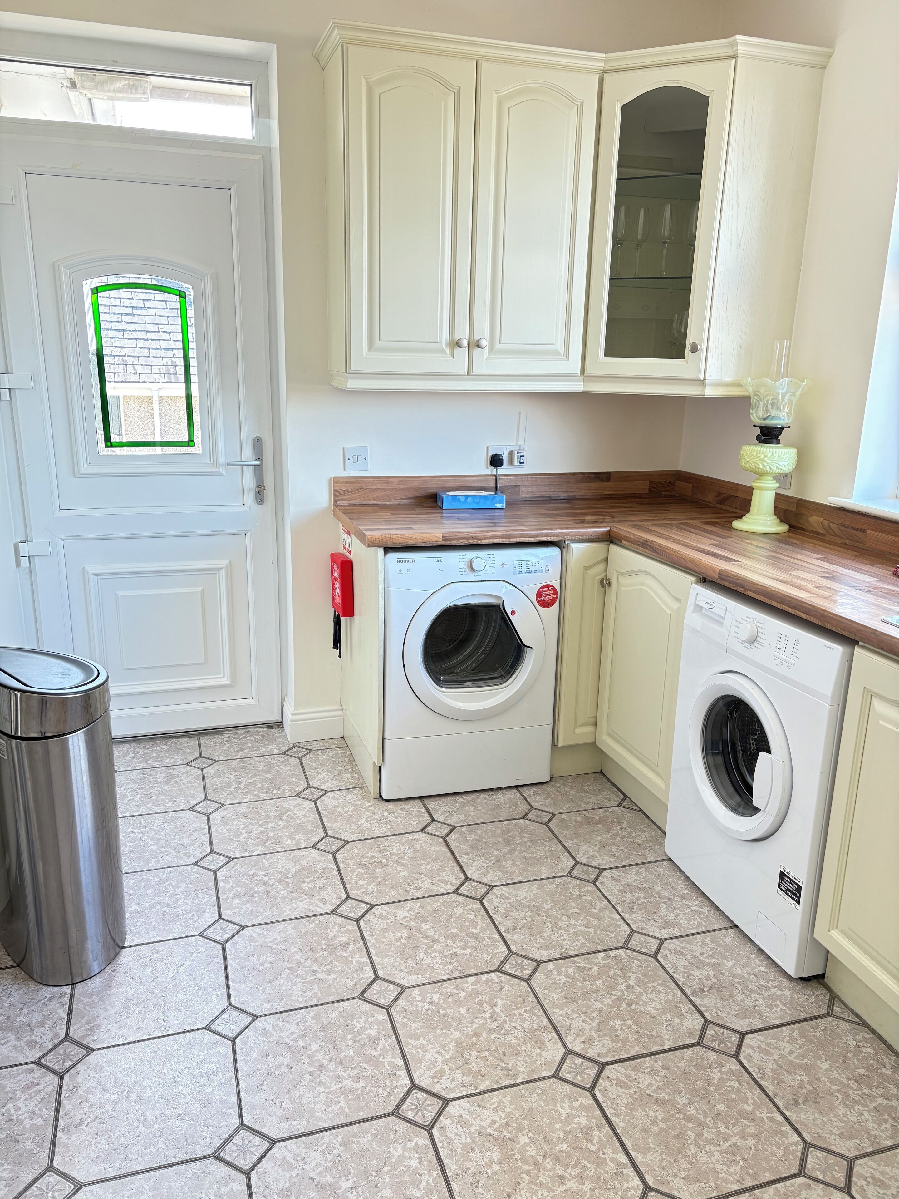 Une cuisine compacte équipée d’un lave-linge, d’une poubelle et d’une fenêtre à cadre vert.