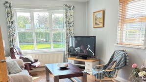 A living room with a sofa, armchair, and a television on a wooden stand. - Peaceful Rural Retreat with Mountain Views - Benbradagh Country Cottage (Dungiven)